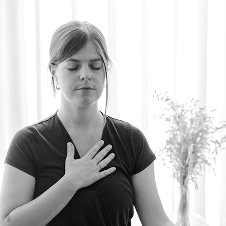 Kelly sitting cross-legged on a mat, eyes closed, one hand resting on her chest