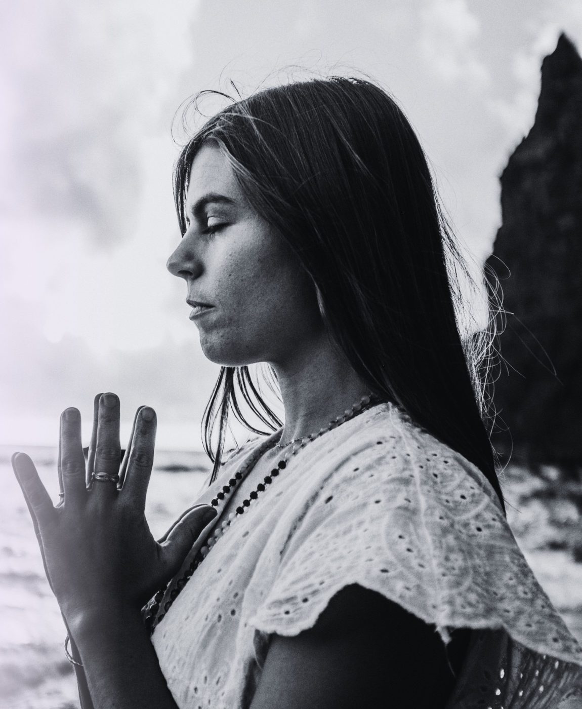 Kelly Fantazi in profile with eyes closed and hands at her heart, by the sea in Madeira