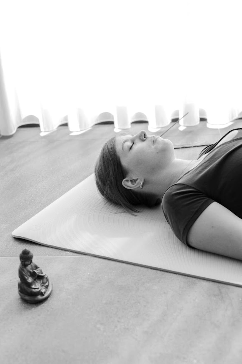 Kelly lying on a yoga mat with her eyes closed, a small Buddha statue nearby
