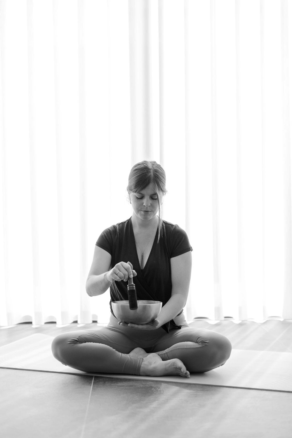Kelly sitting cross-legged, playing a singing bowl in a bright, calm room