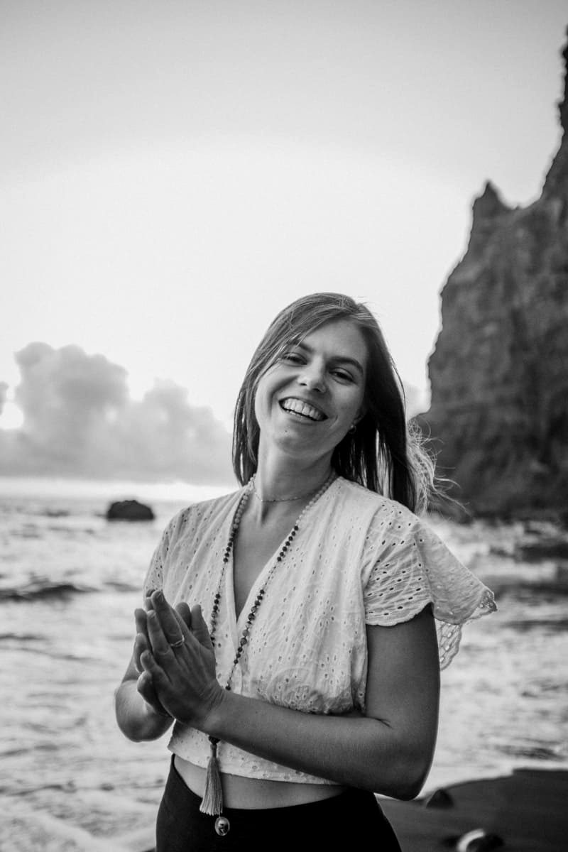 Portrait of Kelly Fantazi smiling by the ocean in Madeira, hands together at her heart