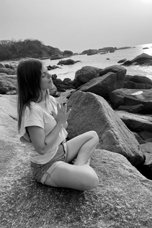 Kelly meditating on rocks by the sea