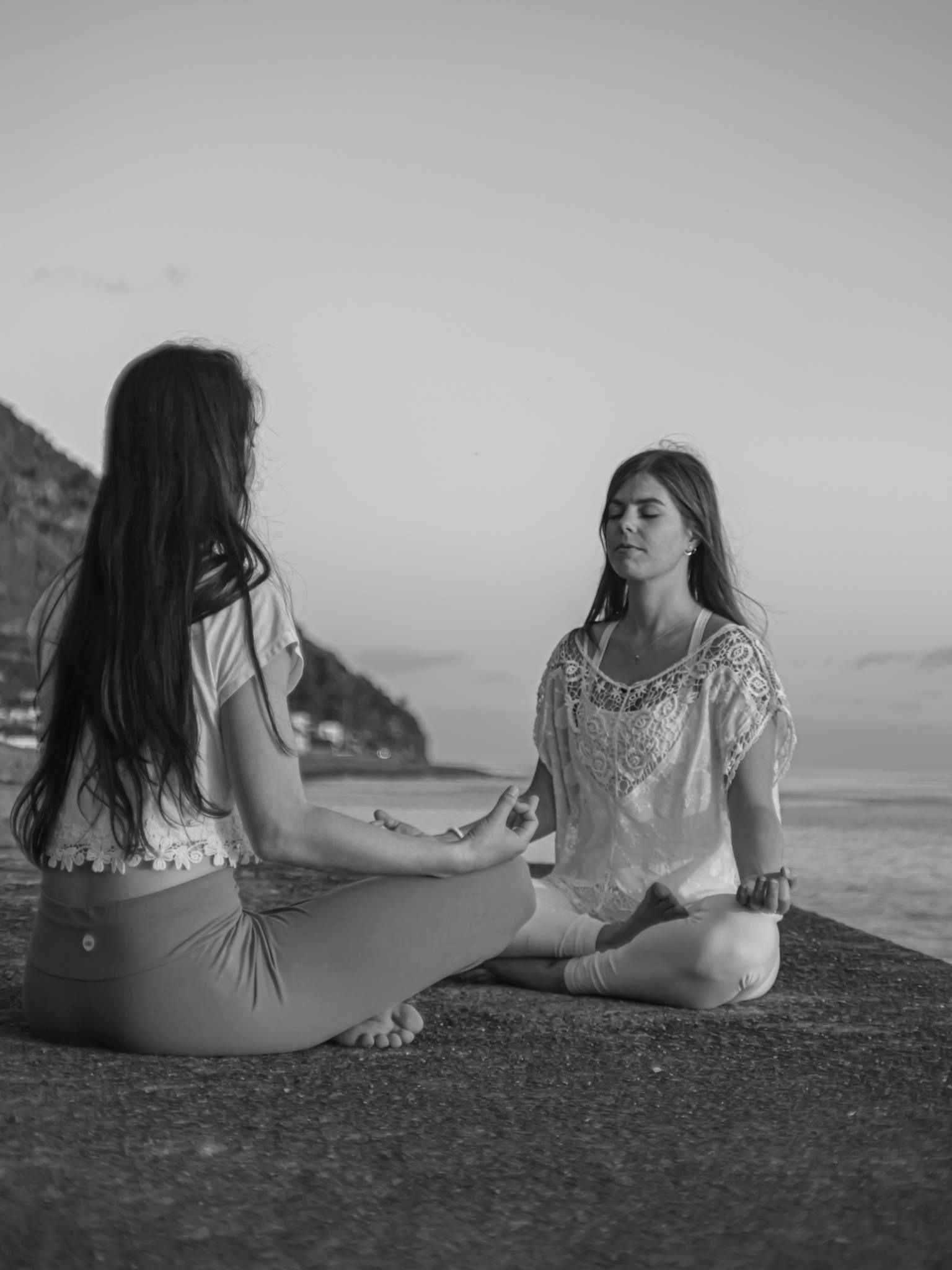 Two women meditating cross-legged on the seafront in Madalena do Mar, Madeira