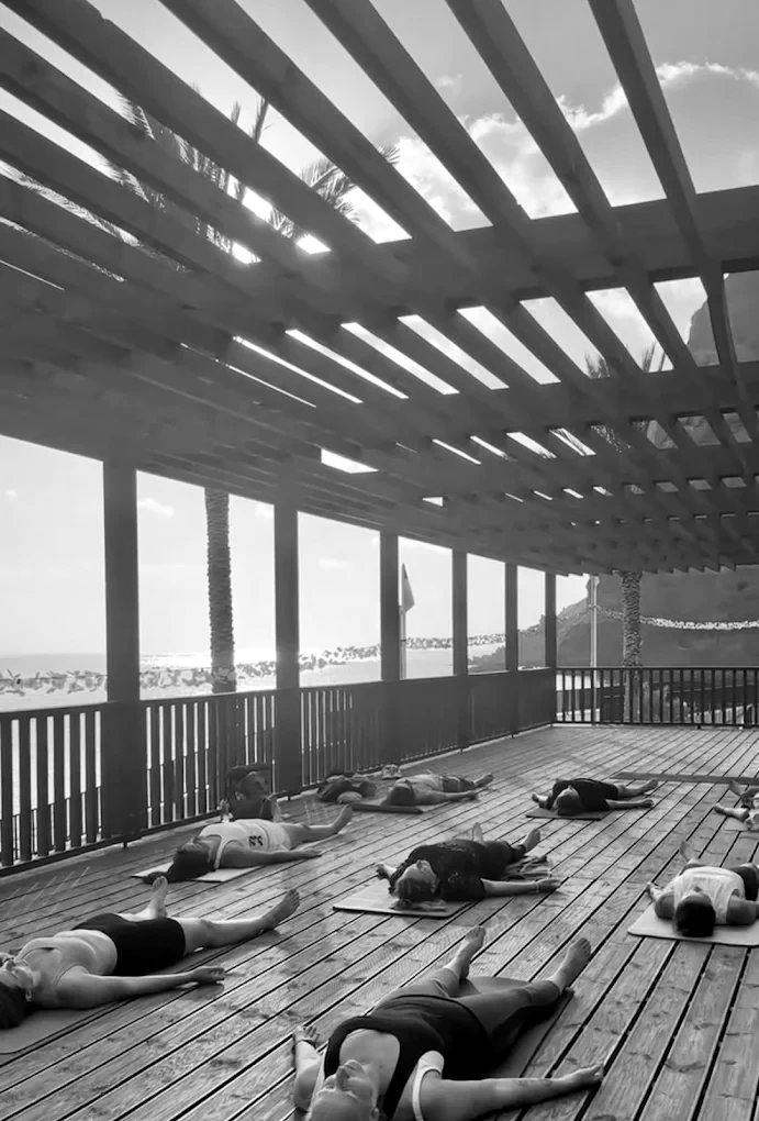 Women resting on yoga mats on a wooden deck by the ocean in Madalena do Mar at sunset